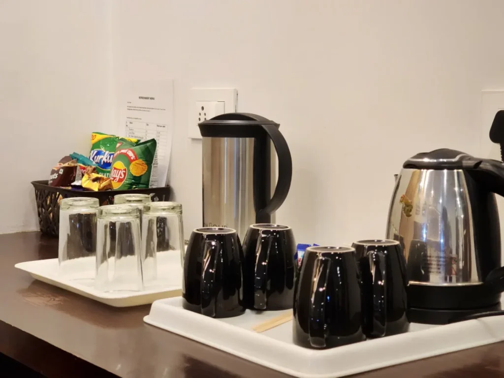 Complimentary tea and coffee maker with electric kettle, cups, glasses, and refreshments in a guest room at Hotel Surya Shimla near Mall Road.