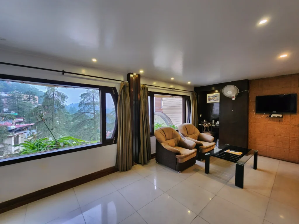 Spacious luxury suite room at Hotel Surya Shimla featuring a comfortable seating area, large panoramic windows with mountain views, modern interiors, and premium amenities near Mall Road.