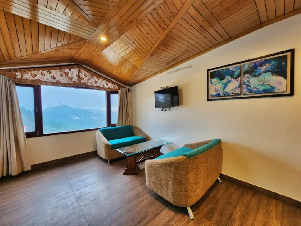 Premium Family Suite at Hotel Surya Shimla featuring a spacious sitting area, wooden ceiling, mountain view window, smart TV, and comfortable sofa seating.